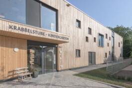 Eingangsbereich von einem Kindergarten mit einer Holzfassade und quadratischen Fenstern 
